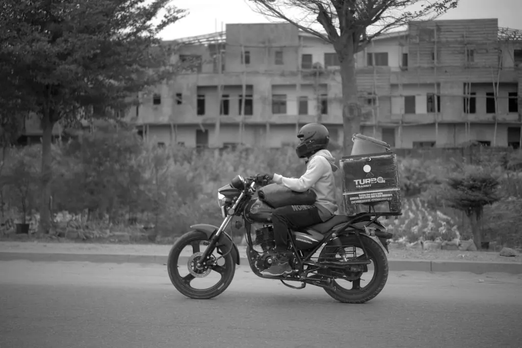 Un livreur casqué roule à moto, une caisse de livraison fixée à l'arrière.